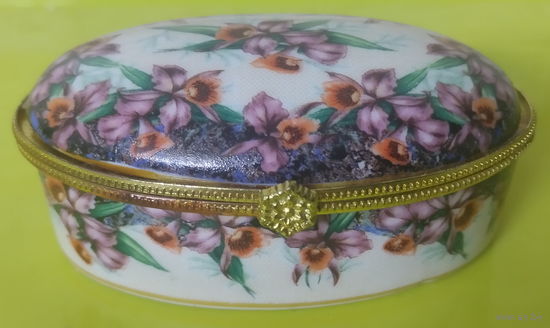 Декоративная фарфоровая шкатулка (или дринкет) овальной формы с цветочным узором, напоминающим орхидеи, и золотистой металлической фурнитурой.